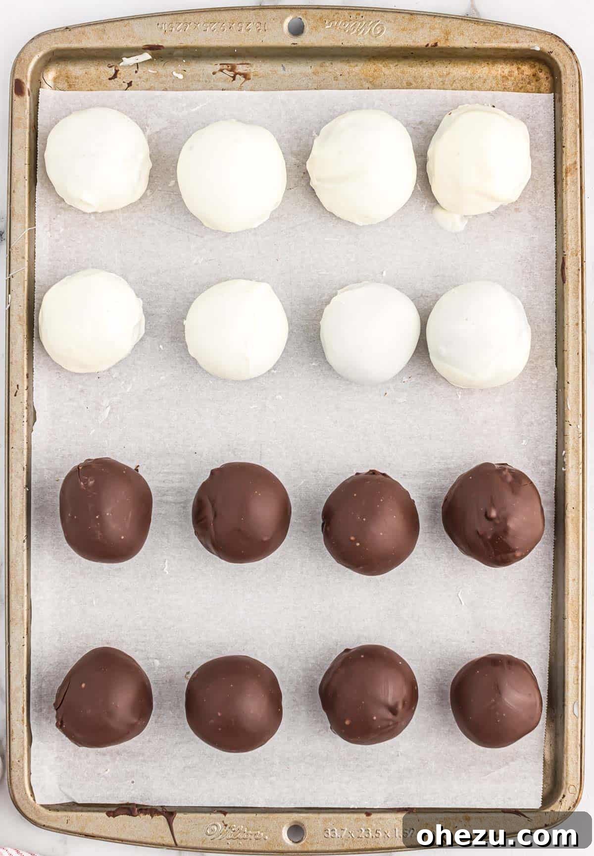 A baking sheet filled with both dark and white chocolate-dipped oreo balls, chilling and hardening.
