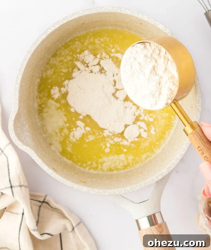 All-purpose flour being gently sprinkled into the melted butter in a saucepan, signaling the beginning of the roux.