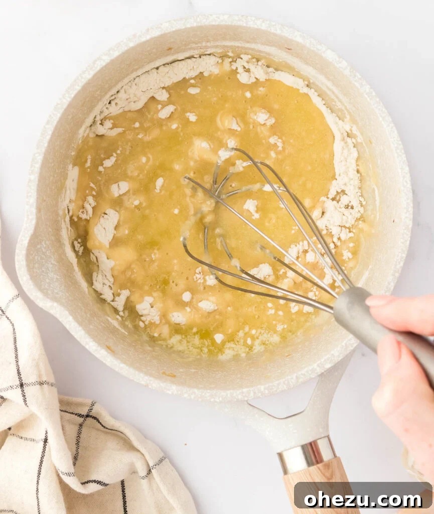 A whisk blending flour into melted butter in a saucepan, creating a smooth, pale roux, free of lumps.