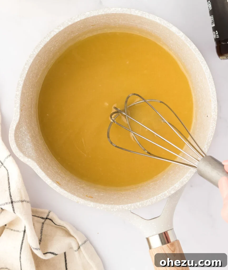 A whisk continuously mixing the roux as vegetable broth and tamari are added, ensuring a smooth, thickening sauce.