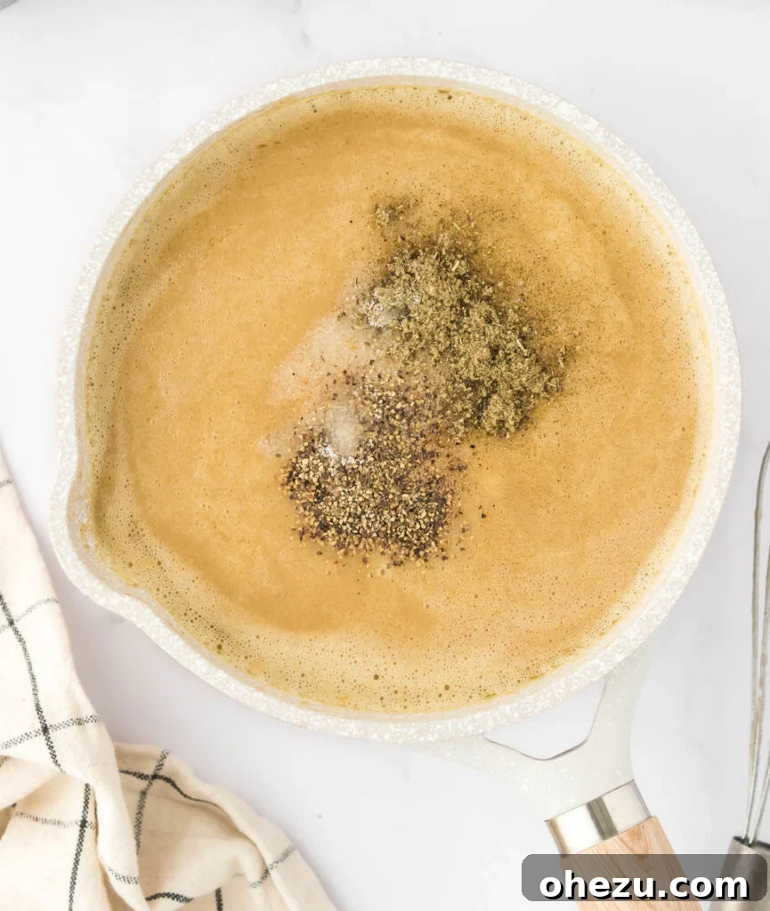 A hand adding a pinch of ground sage to the simmering mushroom gravy in a saucepan, infusing holiday aroma.