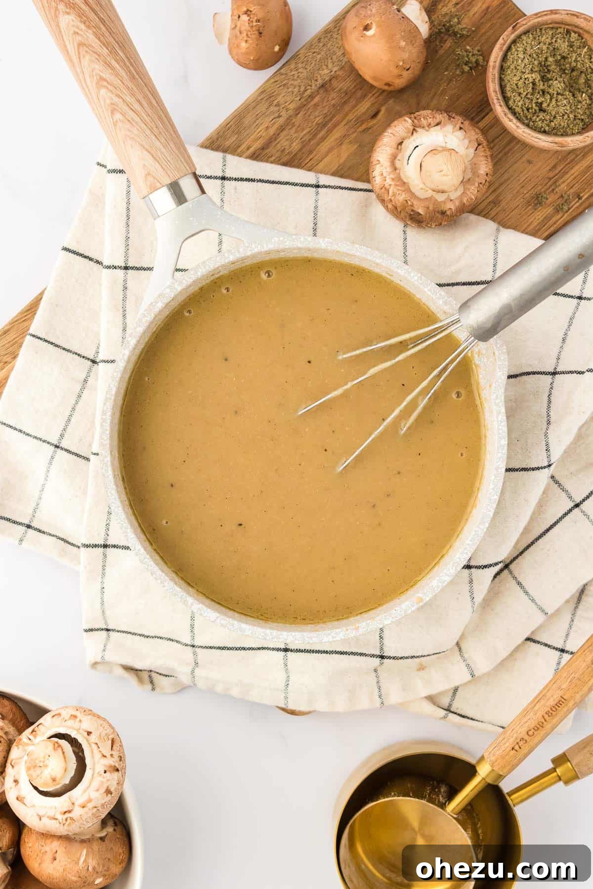 A person expertly whisking rich, brown vegetarian gravy in a stainless steel saucepan over a stovetop burner, ensuring a perfectly smooth and consistent texture.