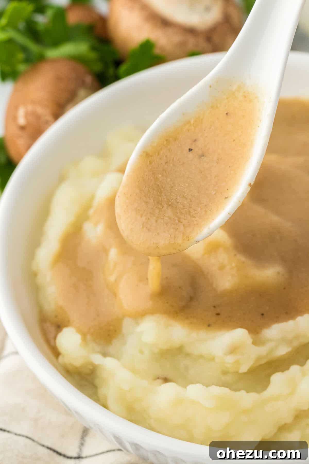 Close-up of a generous serving of vegetarian gravy beautifully poured over fluffy mashed potatoes, delicately garnished with fresh herbs, presented on a pristine white plate.