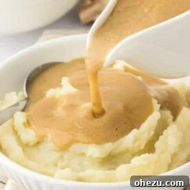 Vegetarian gravy being poured over mashed potatoes on a plate, ready for serving.