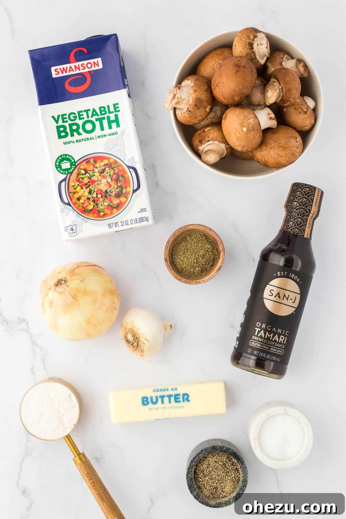 A selection of fresh ingredients including whole baby bella mushrooms, a halved onion, garlic cloves, and a stick of butter, artfully arranged on a wooden cutting board, ready for the vegetarian gravy preparation.