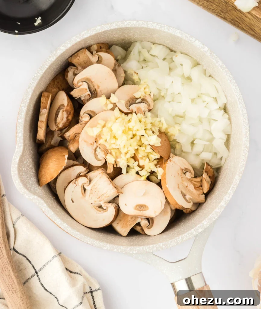 Sautéed mushrooms, garlic, and onion sizzling gently in a saucepan, beginning to cook down and brown.