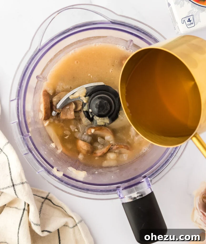 A steady stream of vegetable broth being poured from a measuring cup into a blender containing the mushroom mixture.