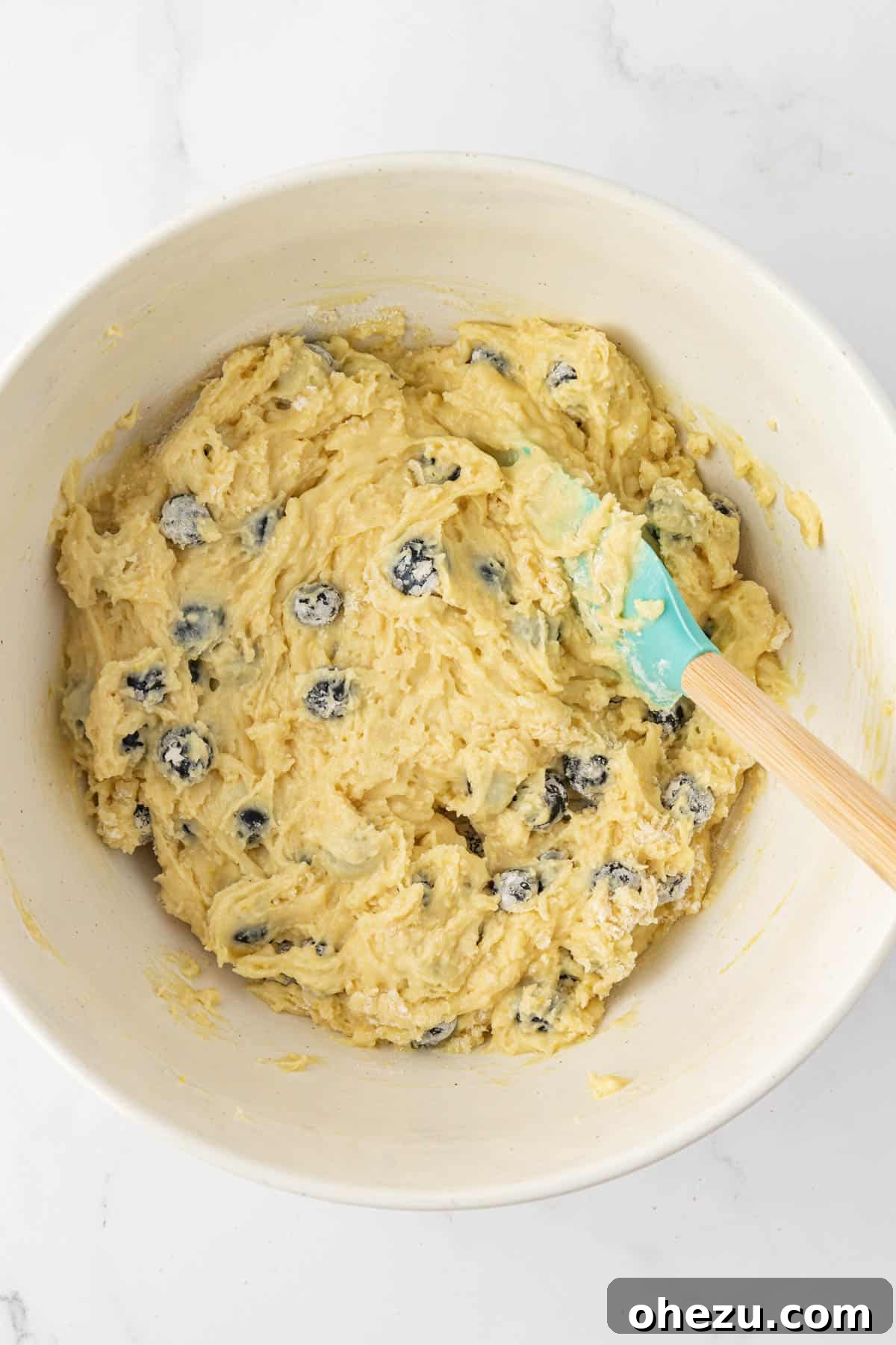 Fresh blueberries gently folded into the muffin batter using a rubber spatula, ensuring even distribution.