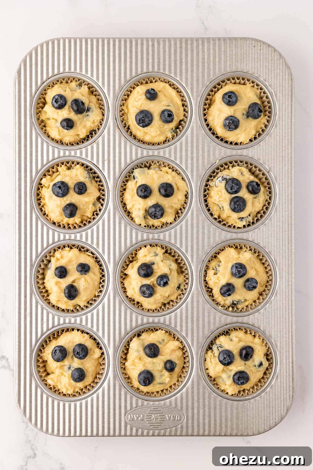 A muffin tin with cups filled with raw sour cream blueberry muffin batter, ready for baking.
