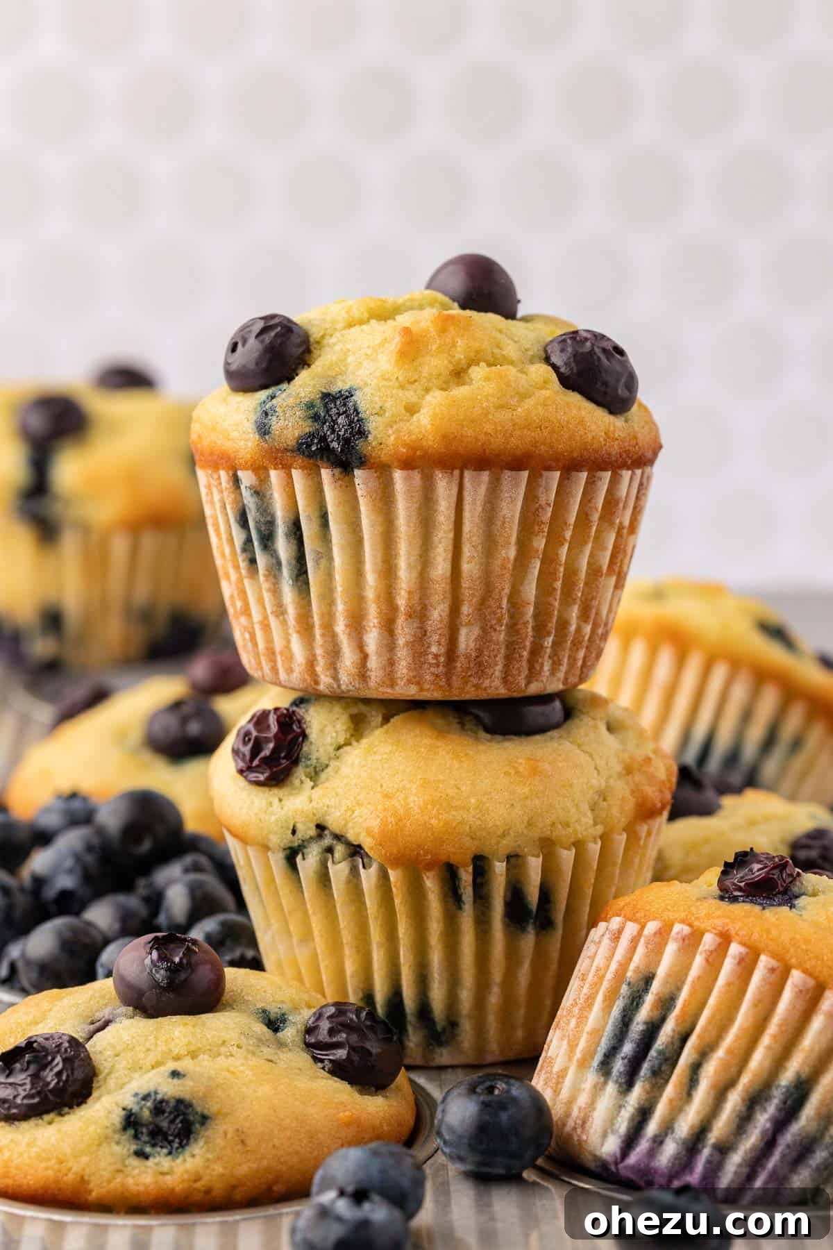 A stack of golden-brown sour cream blueberry muffins on a white plate, ready to be enjoyed.