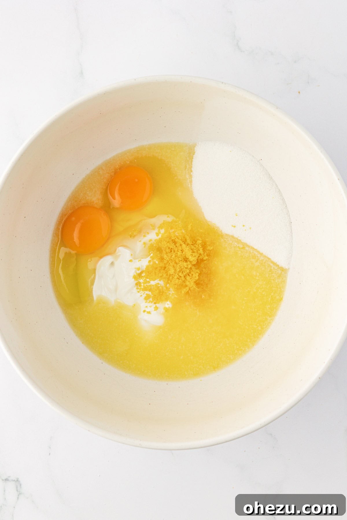 Bowl containing wet ingredients like sour cream, sugar, eggs, melted butter, and lemon zest before whisking.