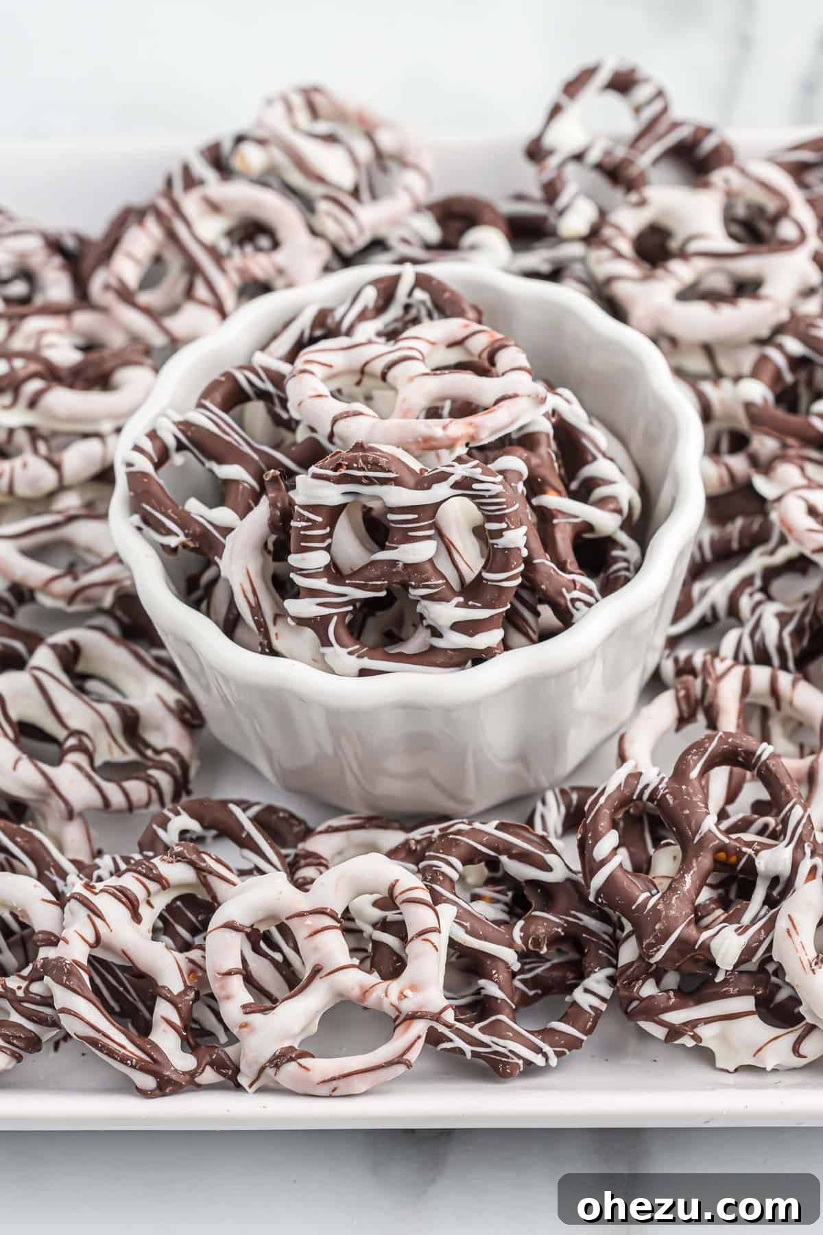A bowl filled with various chocolate covered pretzels, some dark chocolate, some white chocolate, and some drizzled with contrasting chocolate, ready to be enjoyed.