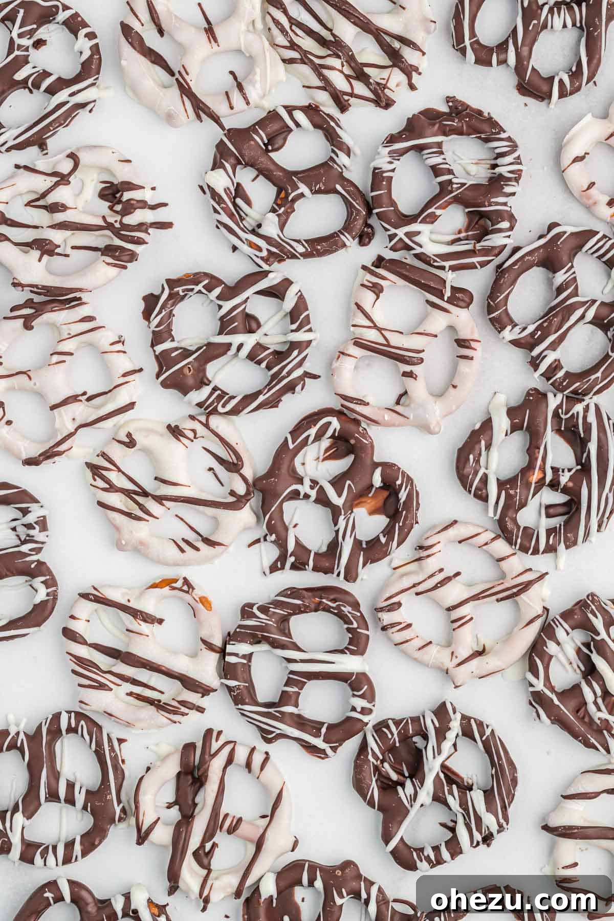 An overhead shot of an assortment of chocolate covered pretzels arranged on a wooden board, featuring both dark and white chocolate coatings with contrasting drizzles.