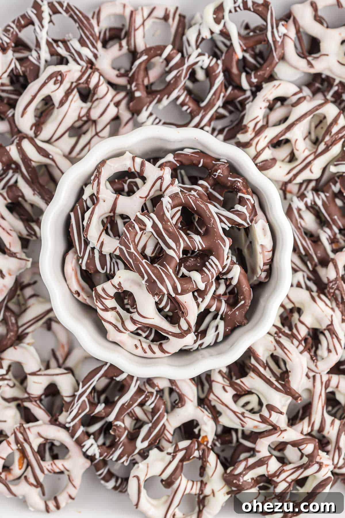 A close-up of beautifully finished chocolate covered pretzels, some with dark chocolate and white drizzles, others with white chocolate and dark drizzles, arranged appealingly.