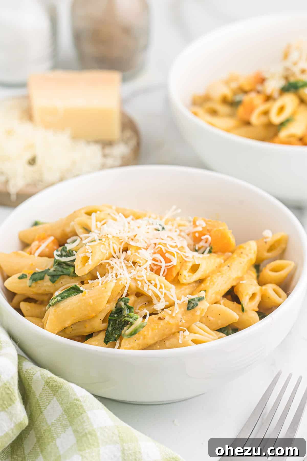 Velvet Sweet Potato Pasta 16 A close-up of sweet potato pasta served in a white bowl, generously topped with freshly grated Parmesan cheese and a sprig of fresh herbs.