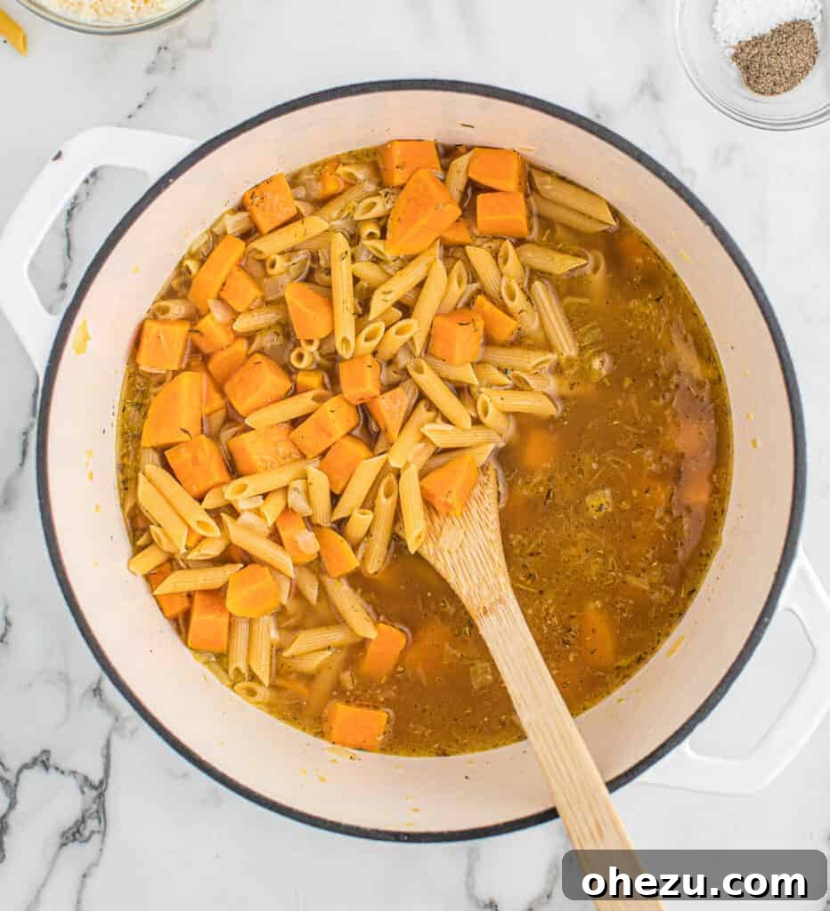 Velvet Sweet Potato Pasta 5 Adding vegetable broth and penne pasta to the sautéed vegetables in the pot.
