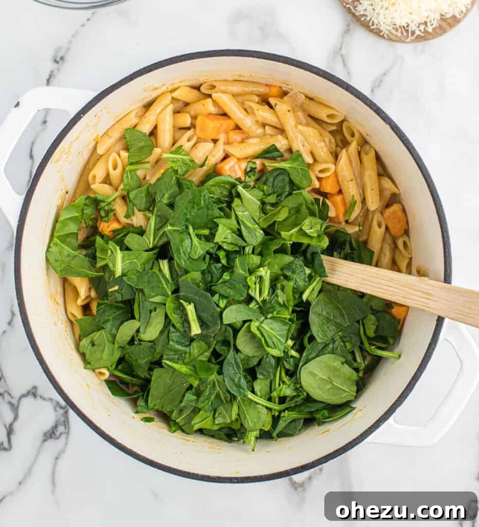 Velvet Sweet Potato Pasta 9 Fresh spinach leaves being added to the creamy sweet potato pasta in the pot.