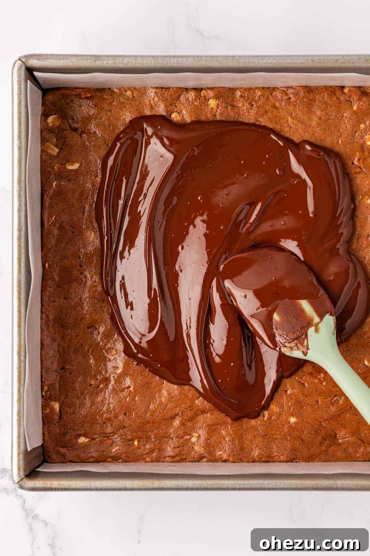 Melted chocolate being smoothly spread over the top of the pressed protein bars in the dish.