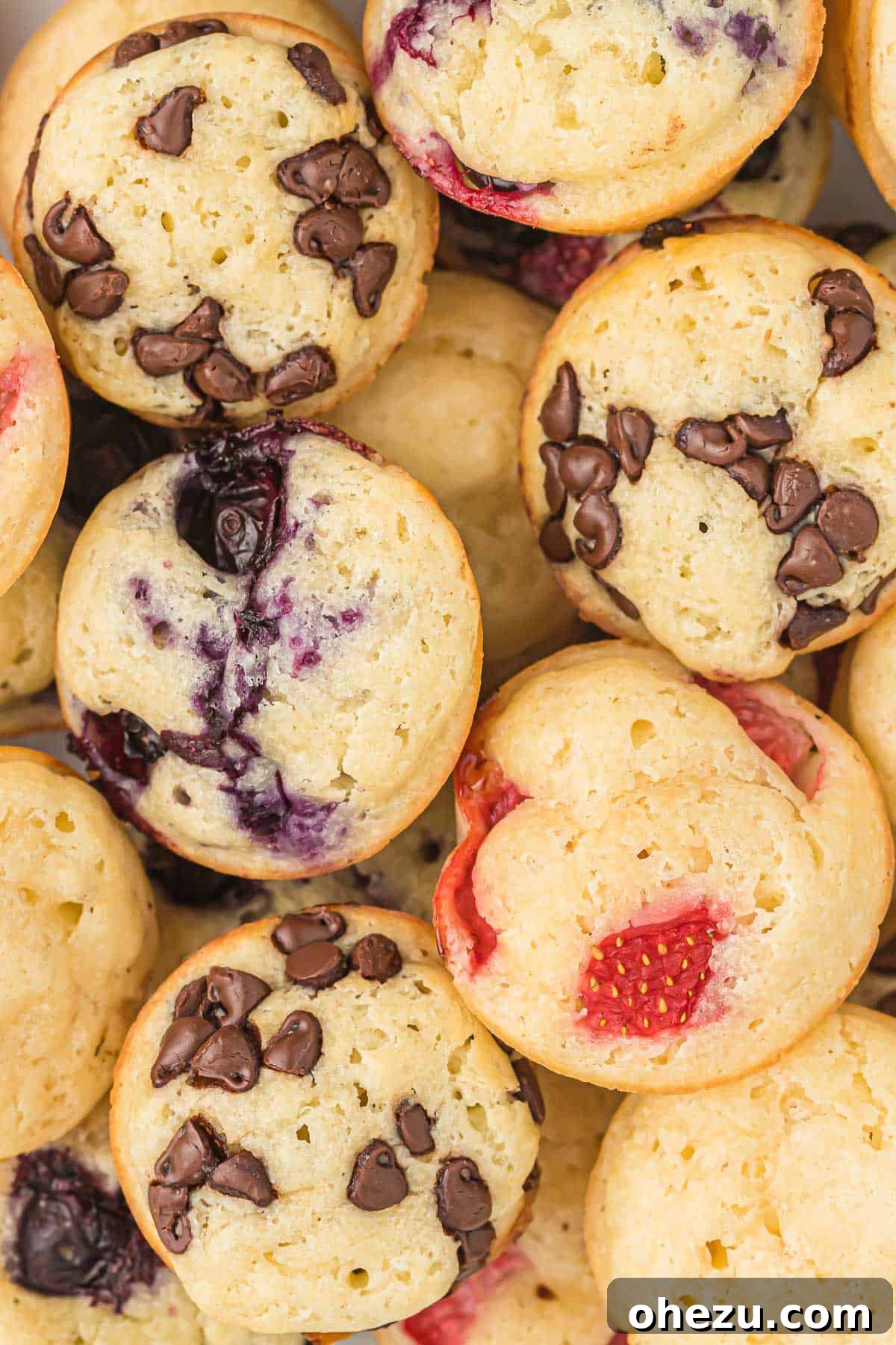Baked Pancake Bites 14 A pile of various pancake mini muffins, featuring different flavors like blueberry, chocolate chip, and plain, on a white background