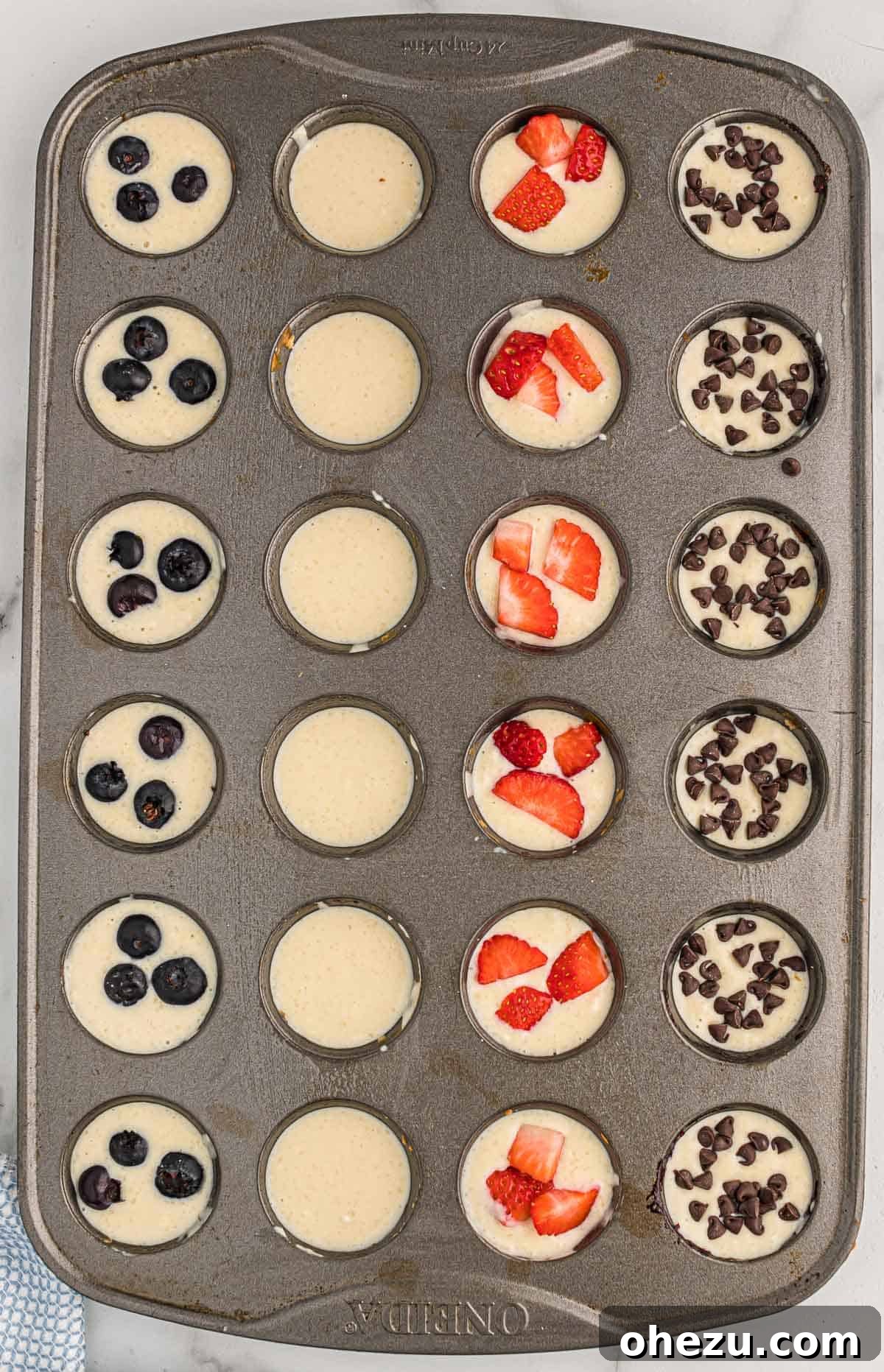 Baked Pancake Bites 9 A mini muffin tin showing different flavored pancake mini muffins before baking: blueberry, strawberry, and chocolate chip