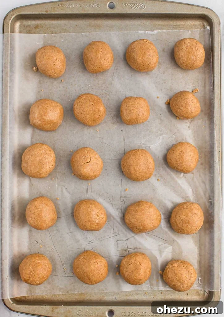 Row of perfectly formed peanut butter balls on a parchment-lined baking sheet