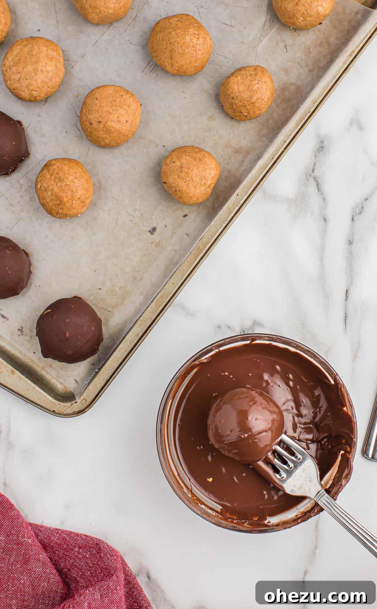 A chilled peanut butter ball being dipped into a bowl of smoothly melted semi-sweet chocolate