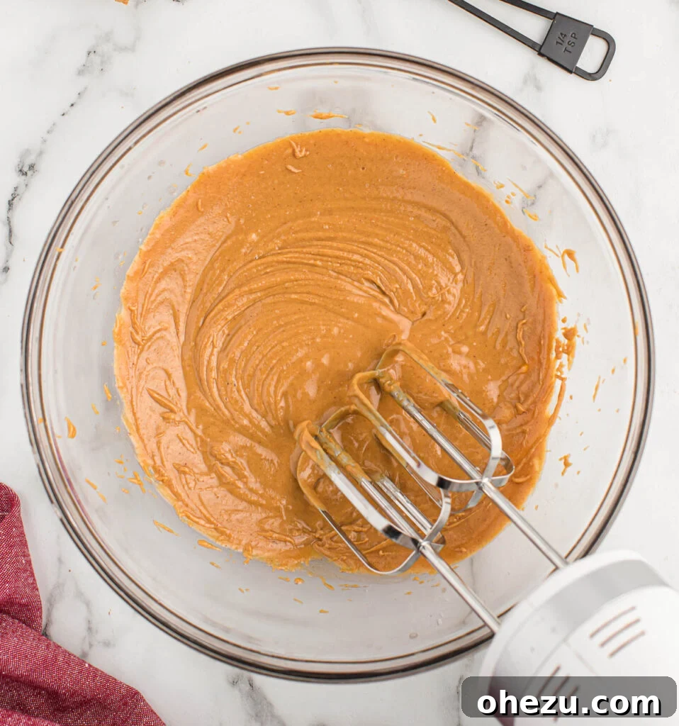 Creamy peanut butter being mixed with melted butter in a stand mixer bowl