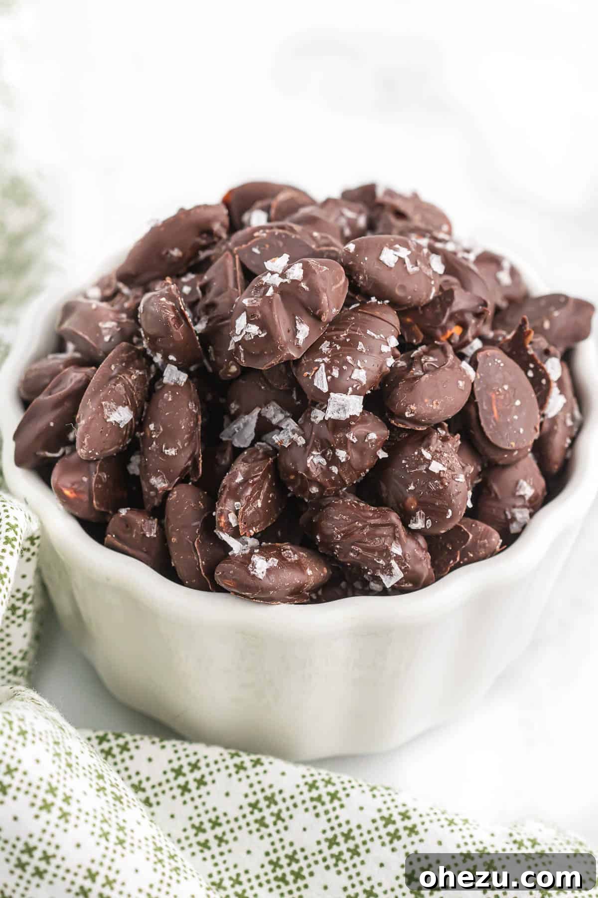 Exquisitely crafted chocolate covered almonds with a sprinkle of sea salt, presented in an elegant white bowl.