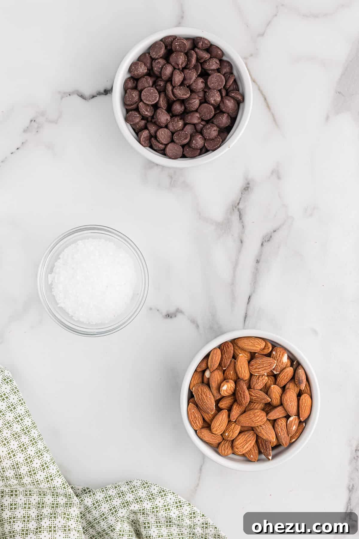 An artfully arranged display of the three key ingredients: raw almonds, rich dark chocolate chips, and sparkling sea salt flakes.