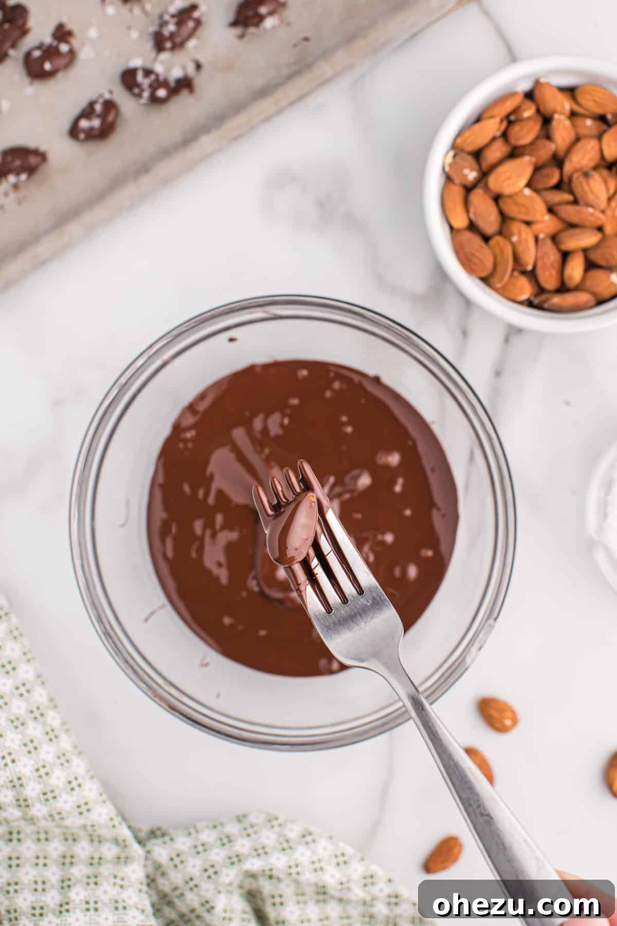 A moment captured: an almond being delicately dipped into a bowl of rich, melted chocolate, ready for its transformation.