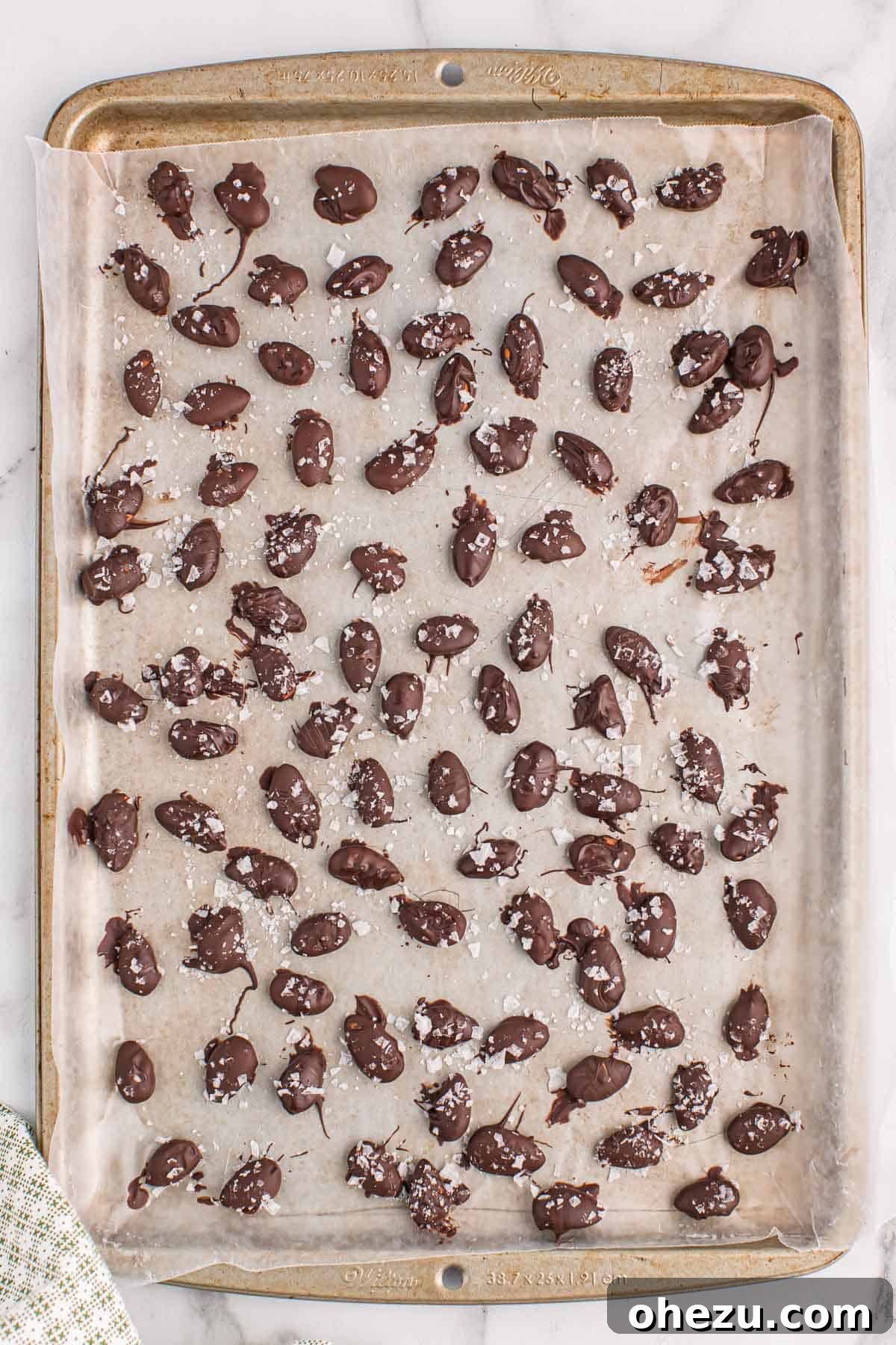 A baking sheet filled with freshly dipped dark chocolate covered almonds, each glistening with a sprinkle of sea salt.