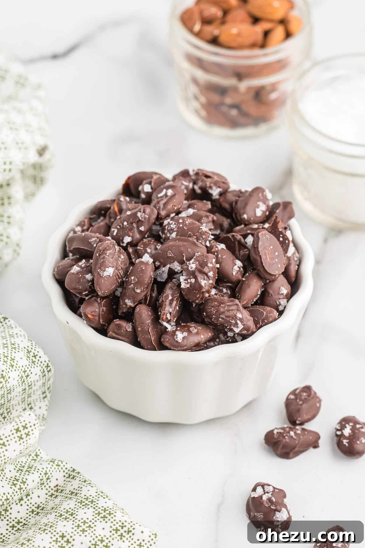 A pristine white bowl overflowing with a generous serving of homemade chocolate covered almonds, perfectly set and ready to be devoured.