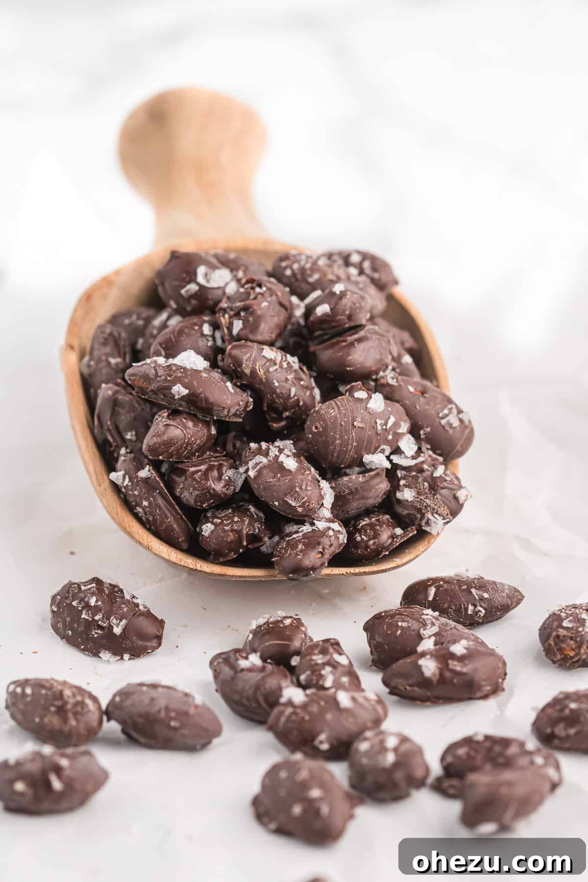 A charming wooden scoop laden with a selection of perfect chocolate covered almonds, highlighting their artisanal appeal.