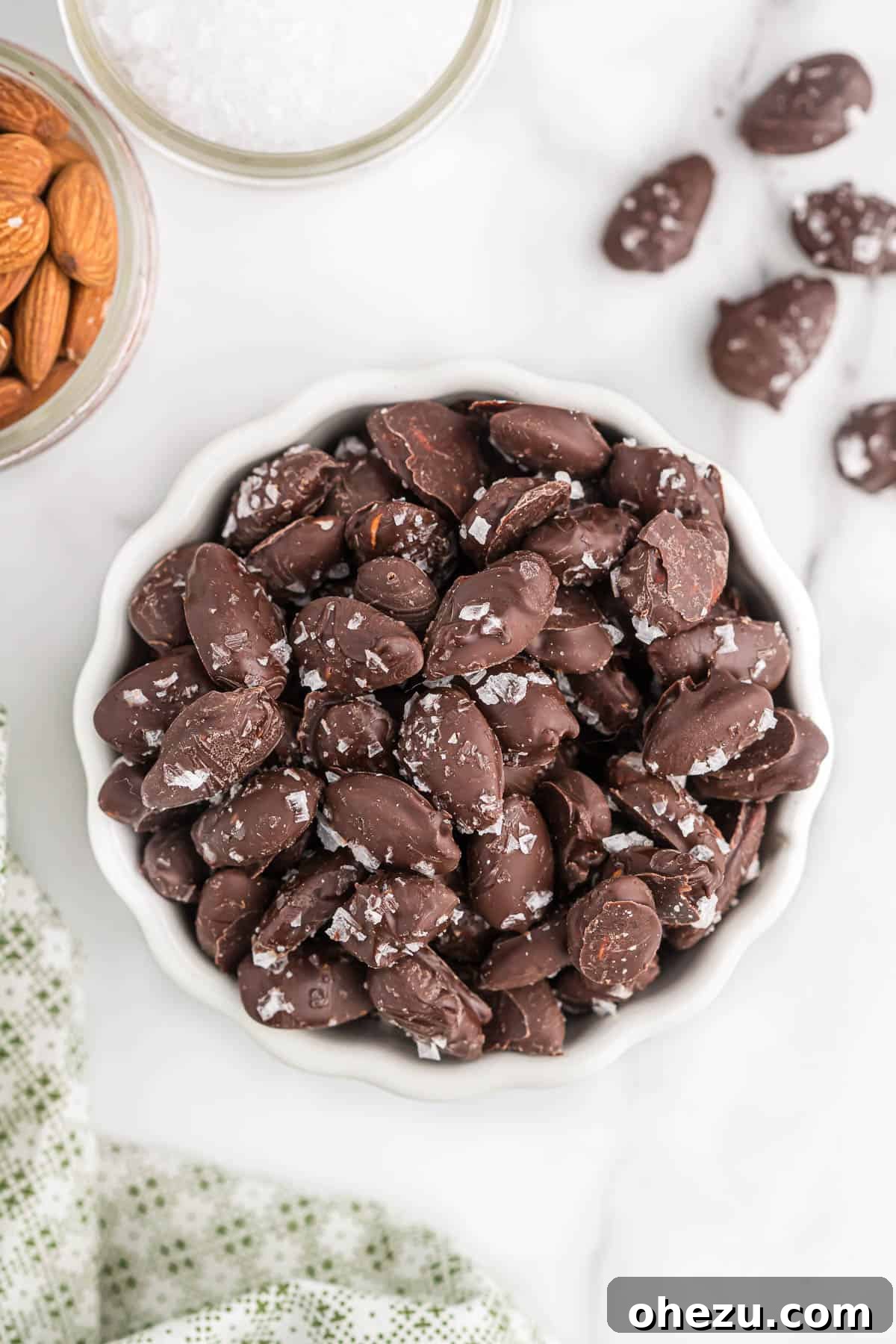 A pristine white bowl overflowing with a generous serving of homemade chocolate covered almonds, perfectly set and ready to be devoured.