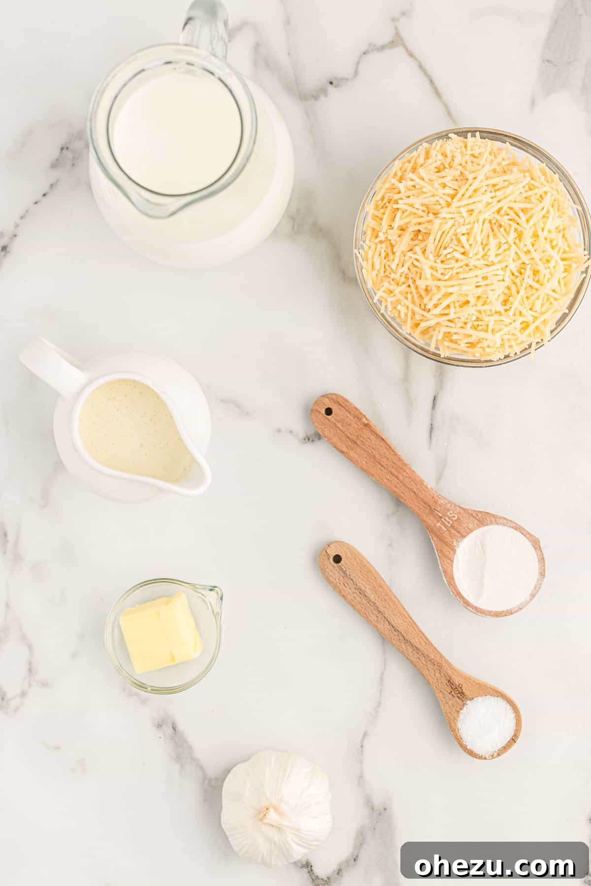 A collection of fresh ingredients laid out, including milk, cream, Parmesan, garlic, butter, and flour.