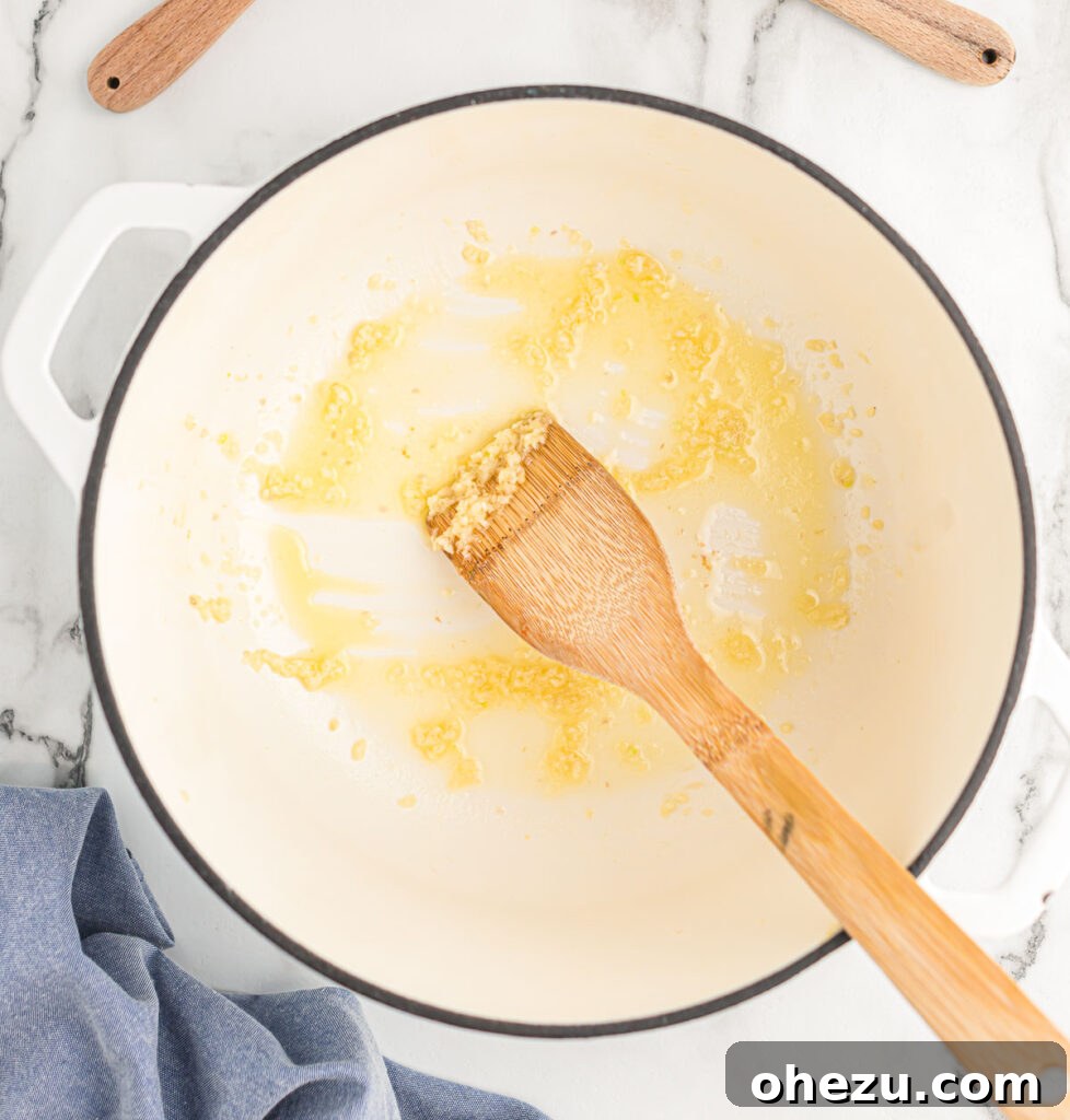 A close-up of minced garlic being stirred in melted butter in a saucepan.