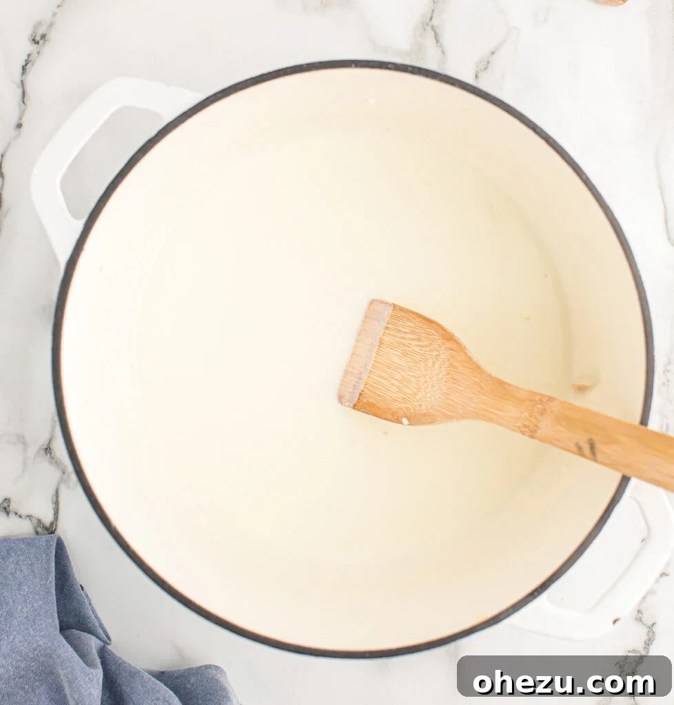 Milk and heavy cream being poured into the saucepan with the roux, creating the creamy base.