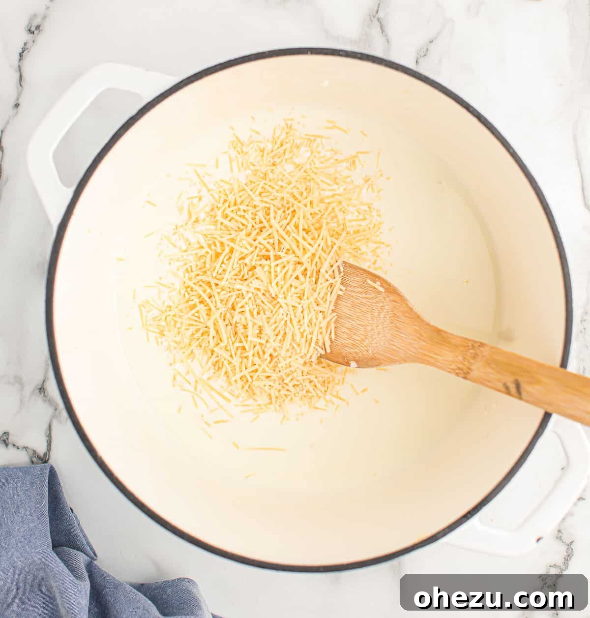 Grated Parmesan cheese being stirred into the hot cream sauce until fully melted and smooth.