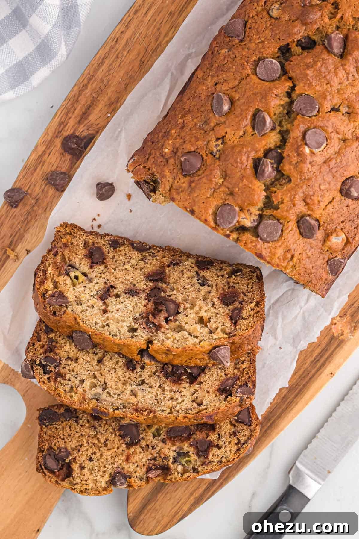 Freshly baked chocolate chip banana bread being cut into thick, inviting slices on a wooden cutting board, revealing its moist texture and rich, melted chocolate chips.