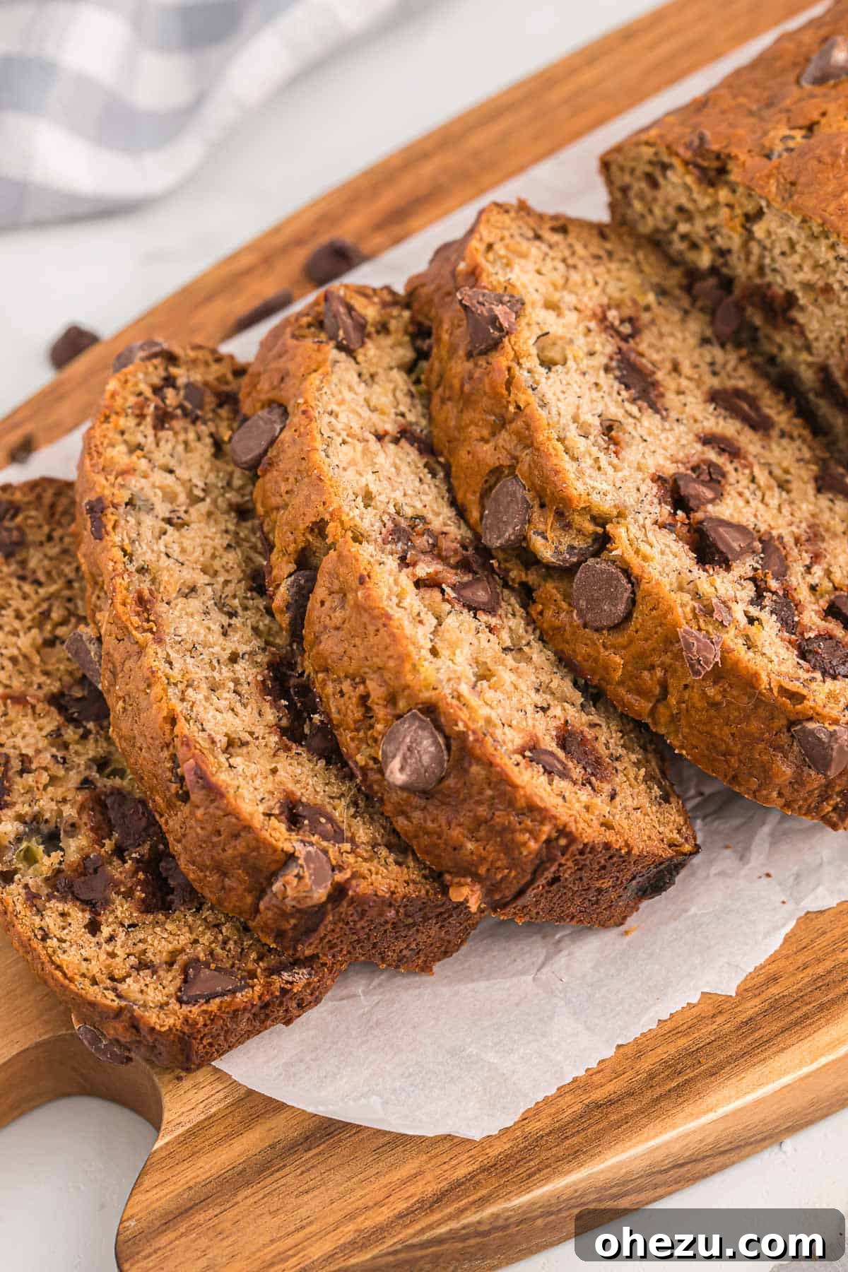 A rustic yet elegant presentation of several golden-brown slices of chocolate chip banana bread on a wooden cutting board, with a clear focus on their appealing texture and generous chocolate chunks.