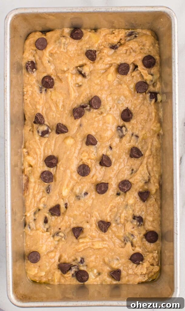 Delicious chocolate chip banana bread batter in a neatly greased loaf pan, adorned with extra chocolate chips on top, patiently awaiting its turn in the oven.