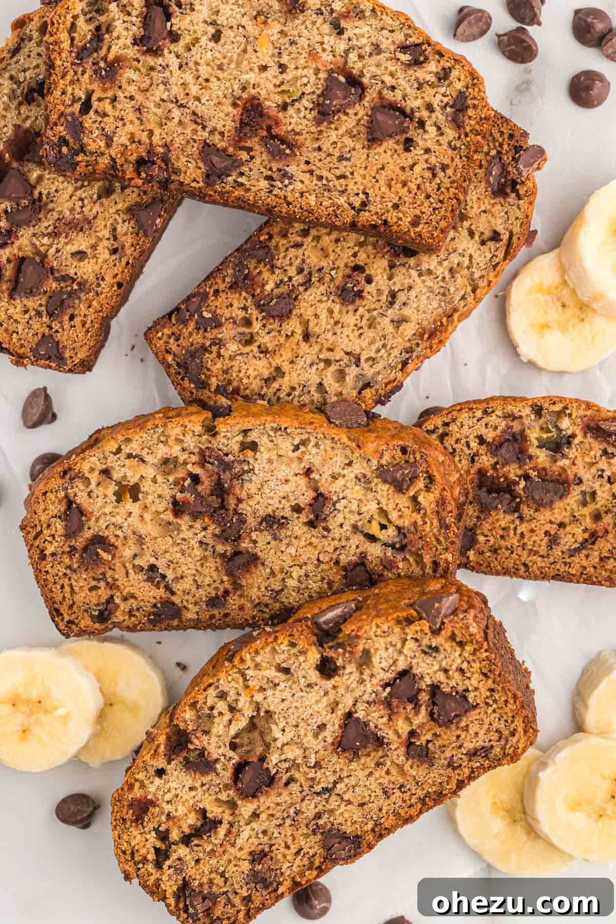 A close-up photograph of a stack of moist, freshly baked chocolate chip banana bread slices arranged invitingly on a rustic wooden board, prominently showcasing their tender texture and abundant melted chocolate chips.