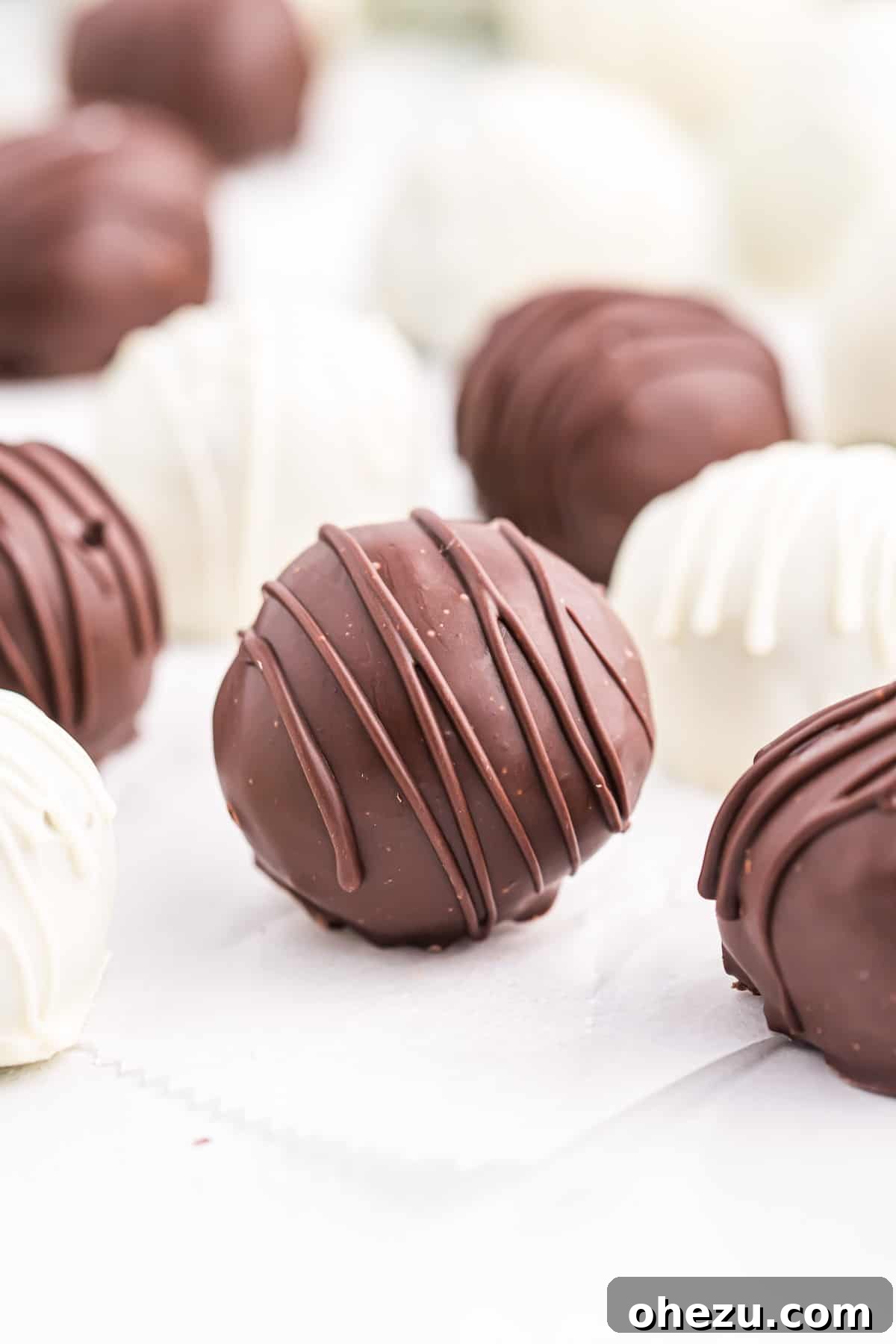 Emerald Oreo Delights 4 A single Mint Oreo Truffle, perfectly round and coated in smooth dark chocolate with a delicate white chocolate drizzle, resting on a parchment-lined baking sheet.