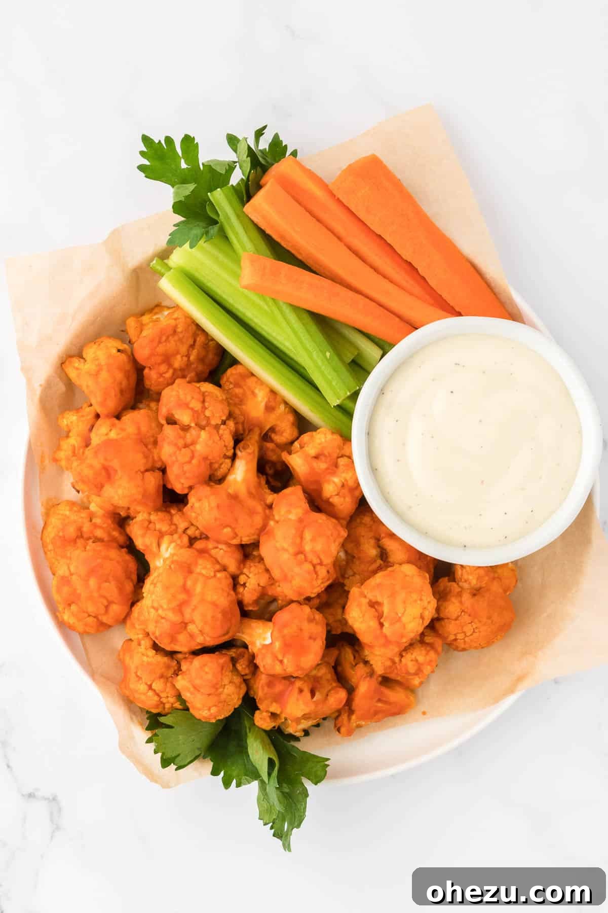 Crispy air fryer buffalo cauliflower bites arranged with fresh celery and carrot sticks, beside a bowl of ranch dressing for dipping.