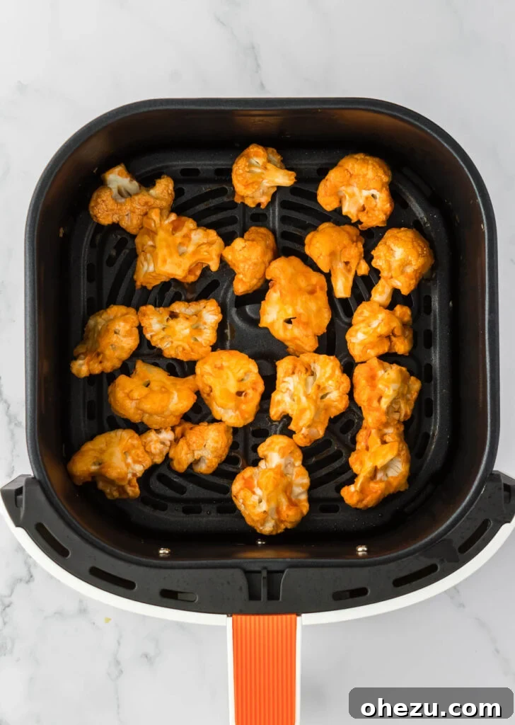 Buffalo-coated cauliflower spread evenly in the air fryer basket for the final round of cooking, to achieve extra crispness and caramelized sauce.