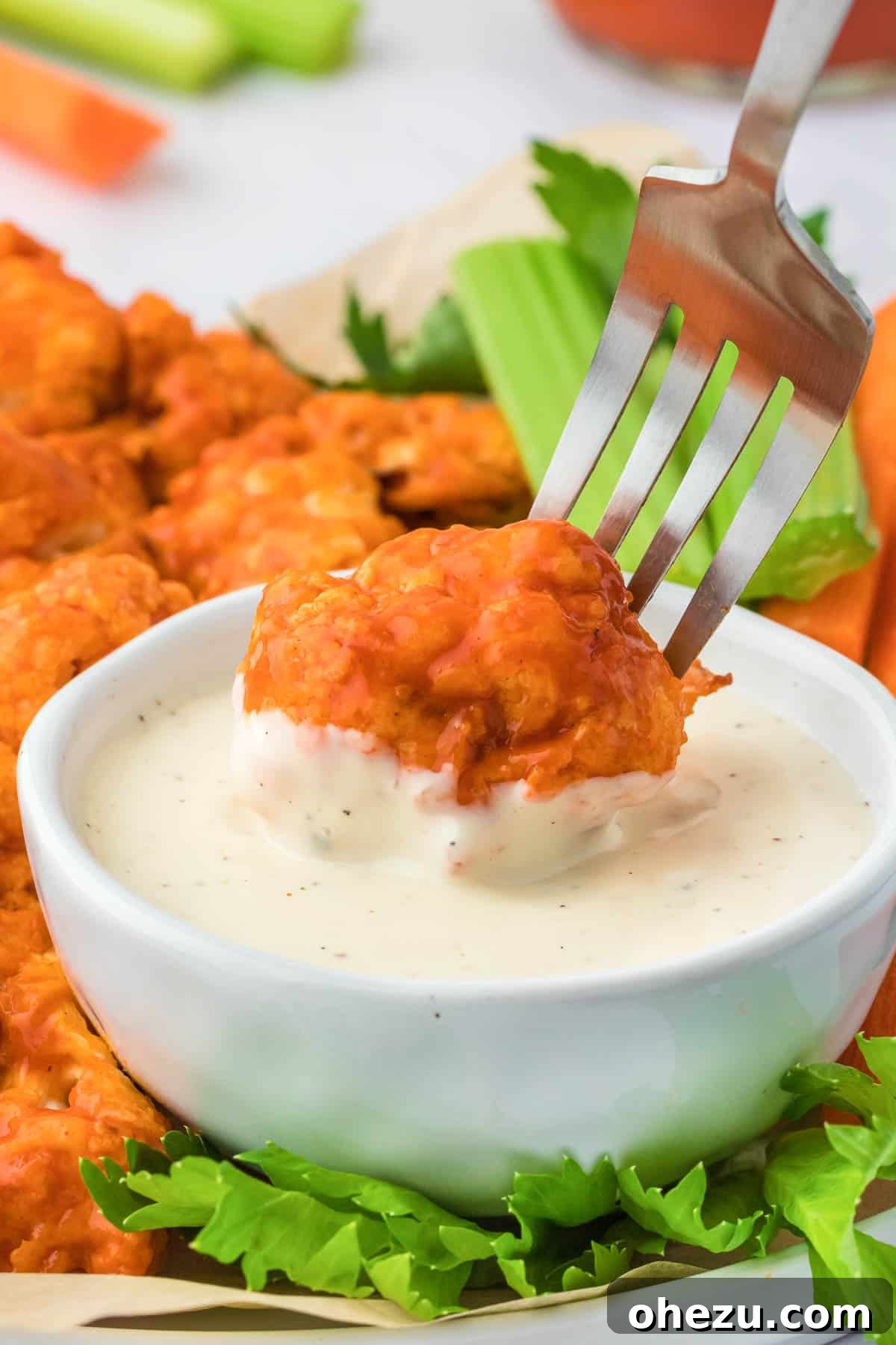 A close-up shot of a crispy, sauce-coated air fryer buffalo cauliflower bite being dipped into a dollop of creamy white ranch dressing in a small bowl.