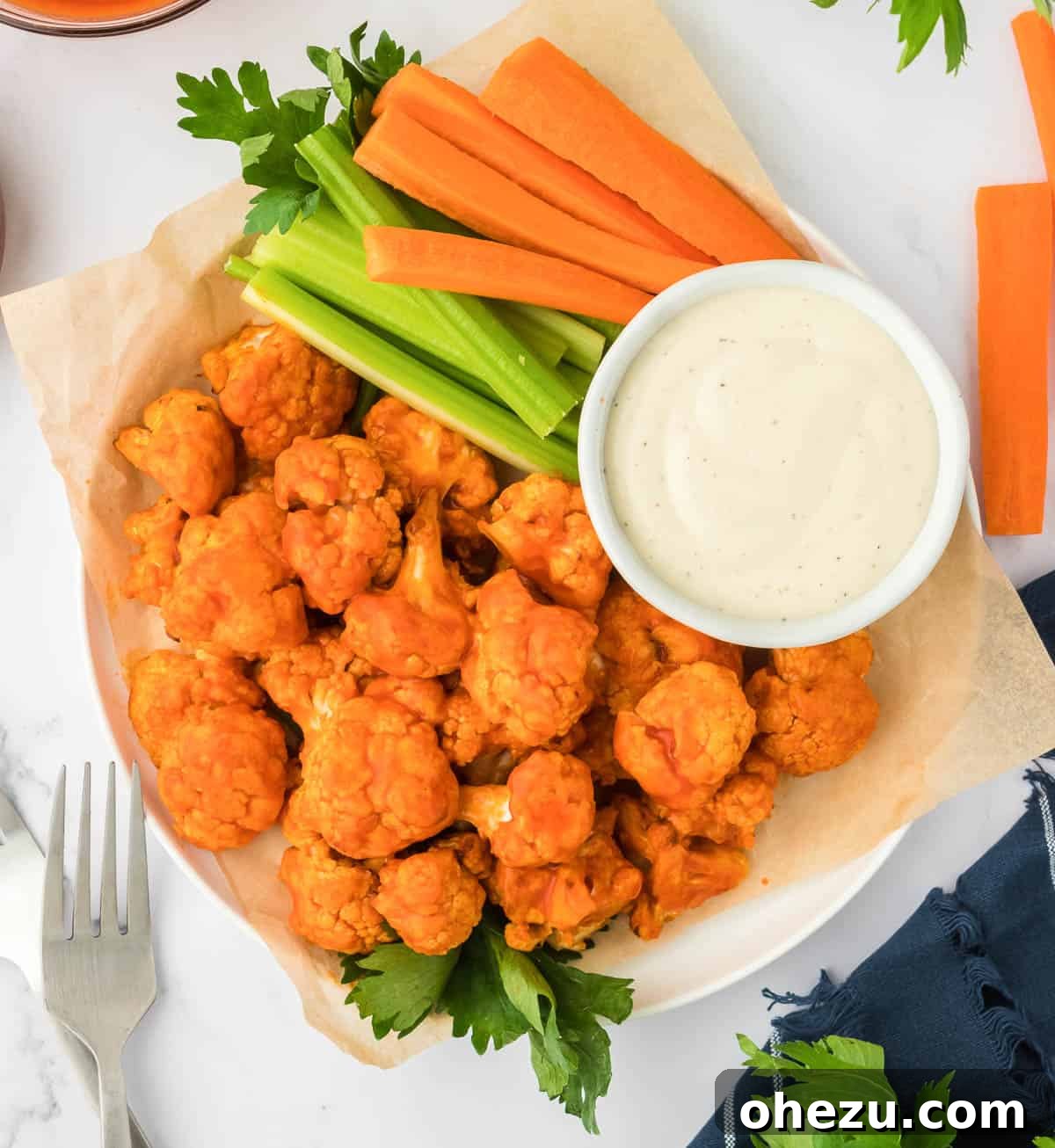 A bountiful platter of air fryer buffalo cauliflower bites, artfully arranged with fresh celery and carrot sticks, and a small bowl of creamy ranch dressing, suggesting a healthy and delicious snack or appetizer spread.