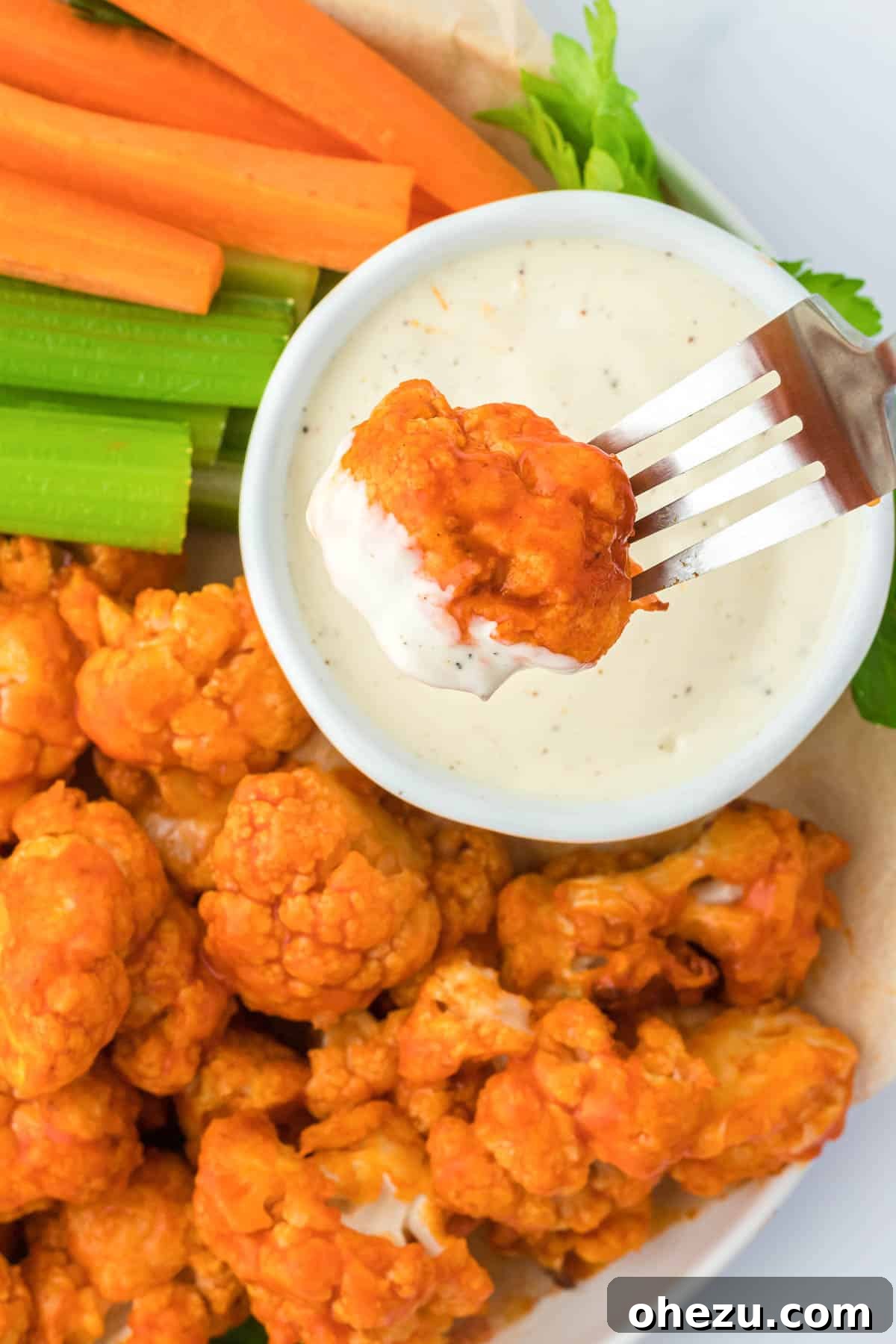 Close-up shot of a single air fryer buffalo cauliflower bite being dipped into a small bowl of creamy ranch dressing.