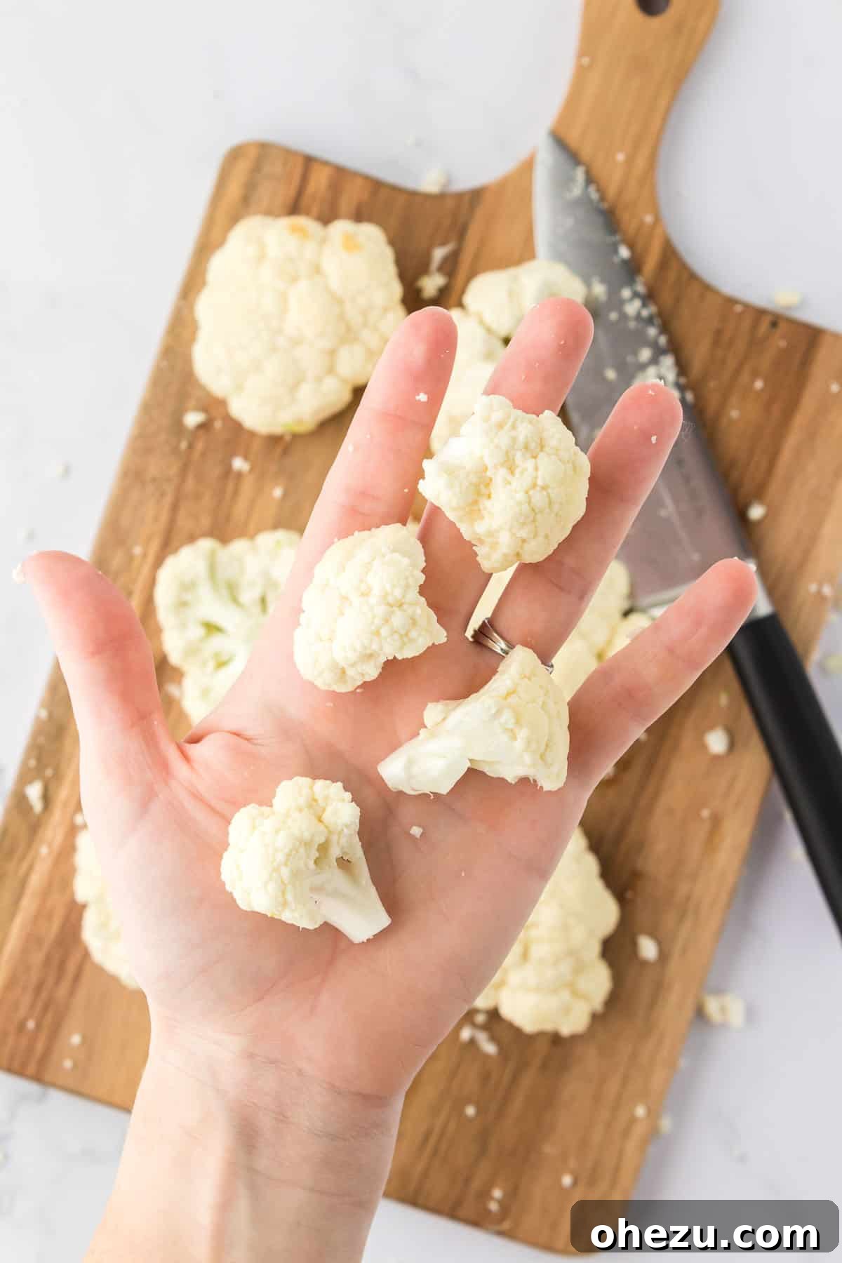 Fresh cauliflower florets, uniformly cut into small, bite-sized pieces, neatly arranged on a cutting board, prepared for the next step of coating.