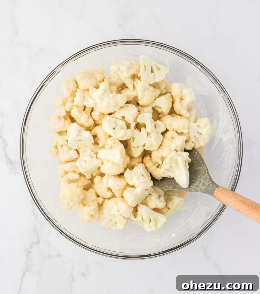 Hands gently tossing cauliflower florets in a mixing bowl, ensuring an even and thorough coating of the flour mixture.